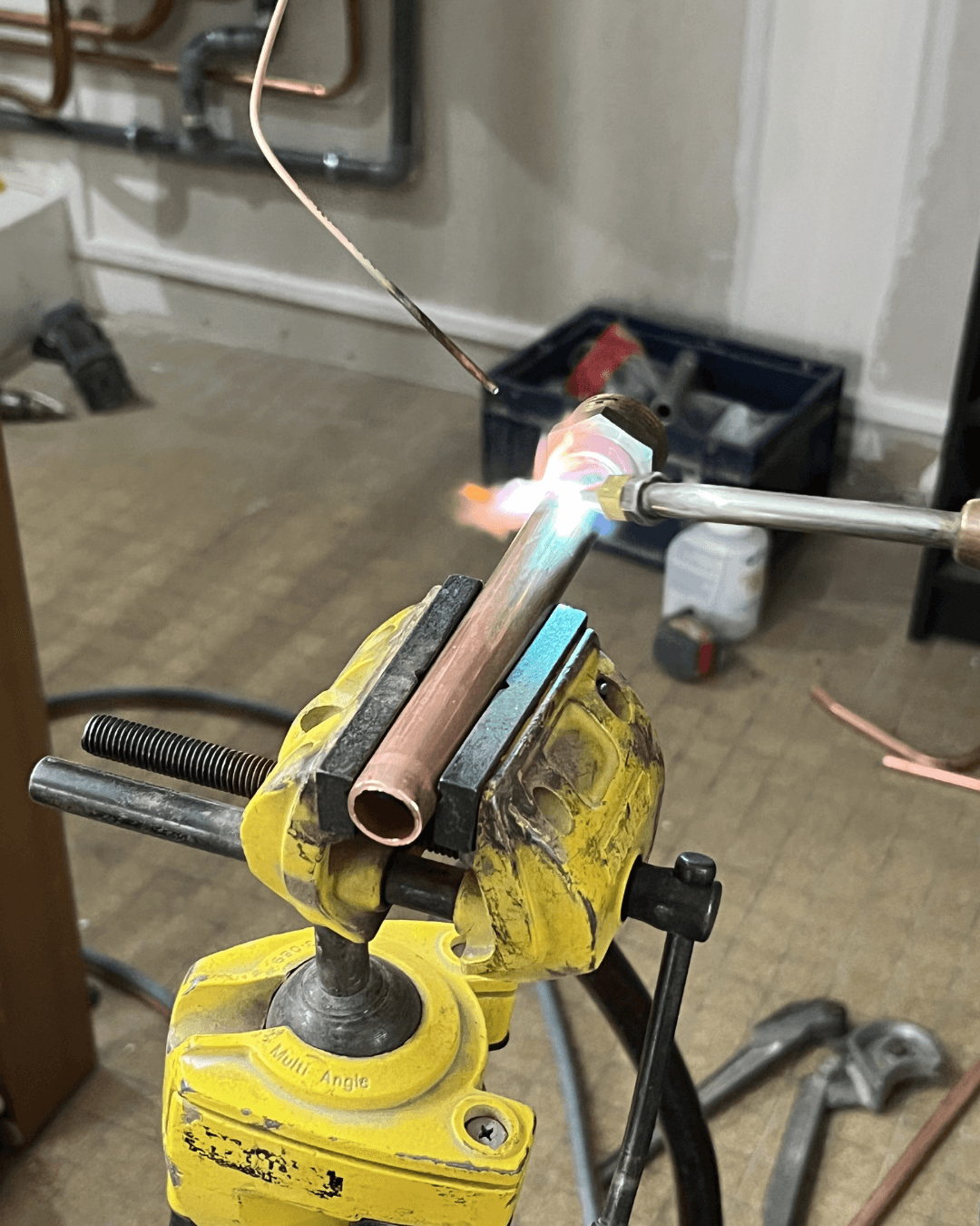 Gros plan sur une opération de brasage de tuyauterie en cuivre dans un étau, étape essentielle pour des réseaux hydrauliques étanches.