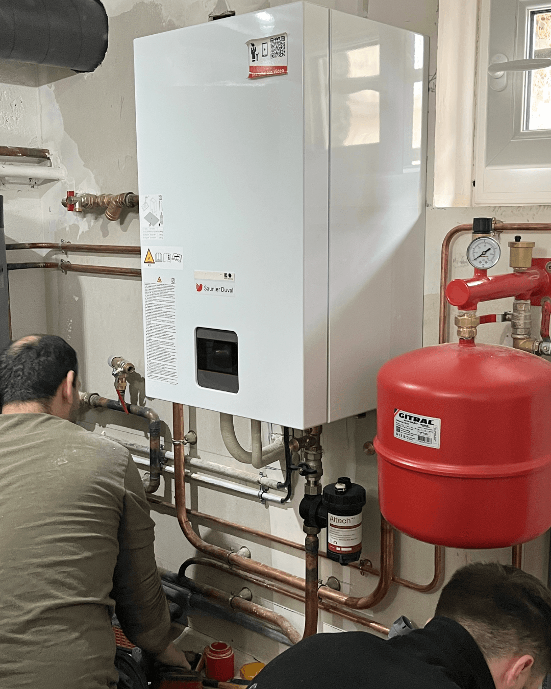 Techniciens chauffagistes LC Thermic réalisant le raccordement hydraulique en cuivre sous l'unité murale de chauffage.