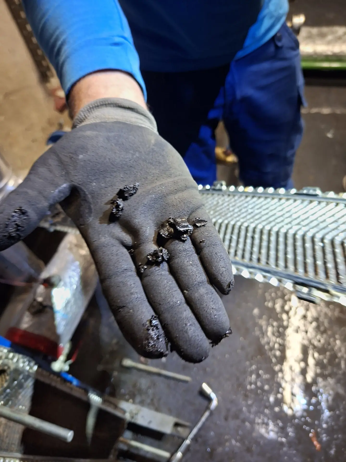 Dépôts de boue extraits de l'échangeur primaire – Copropriété Torcy Gant de technicien recouvert de dépôts de boue noire extraits de l'échangeur primaire d'une chaufferie de copropriété à Torcy – LC THERMIC