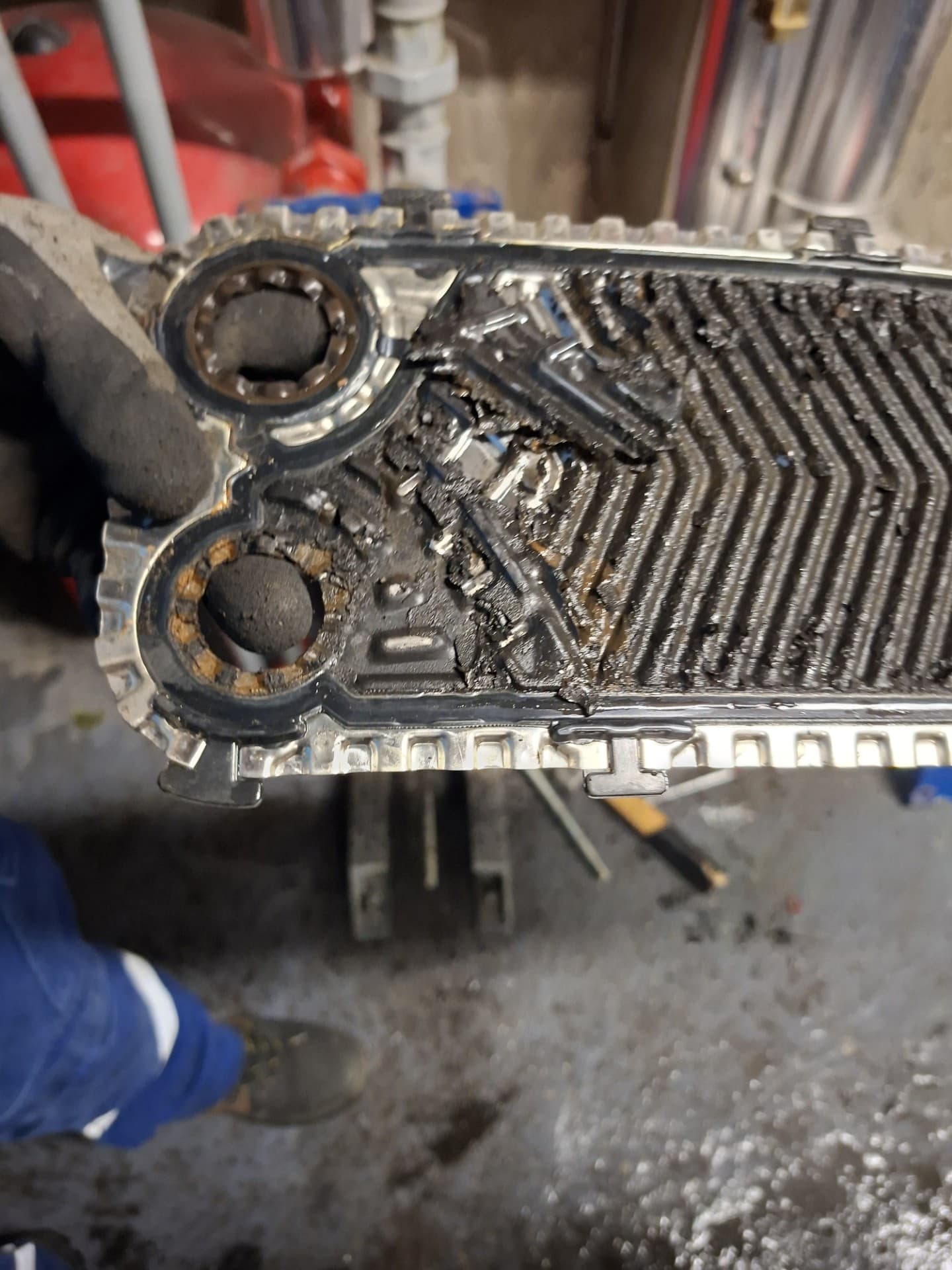 Plaque d'échangeur primaire totalement obstruée par la boue – LC THERMIC Plaque d'échangeur thermique primaire entièrement recouverte de dépôts de boue noire dans une chaufferie de copropriété – chantier Torcy par LC THERMIC