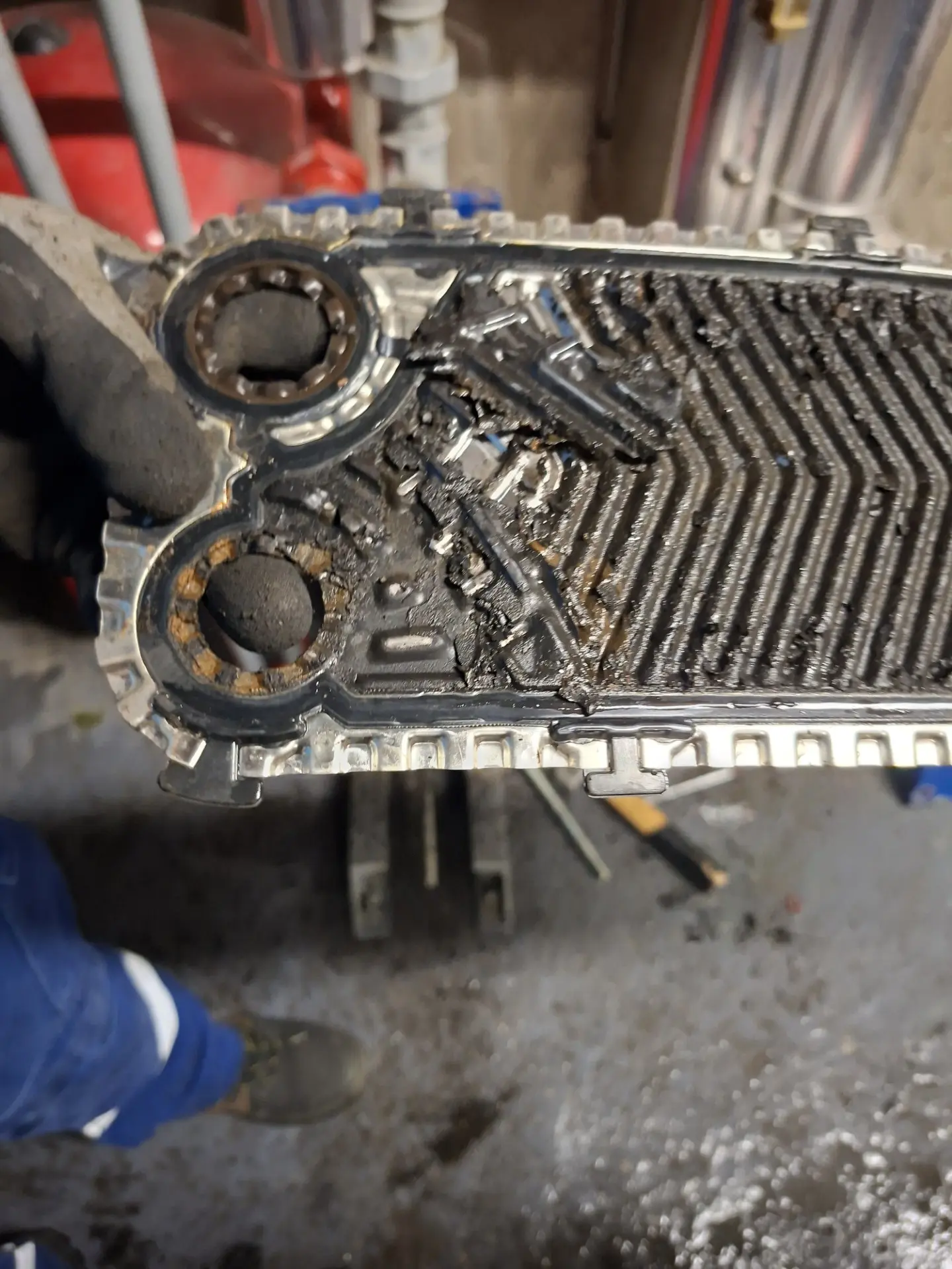 Plaque d'échangeur primaire totalement obstruée par la boue – LC THERMIC Plaque d'échangeur thermique primaire entièrement recouverte de dépôts de boue noire dans une chaufferie de copropriété – chantier Torcy par LC THERMIC